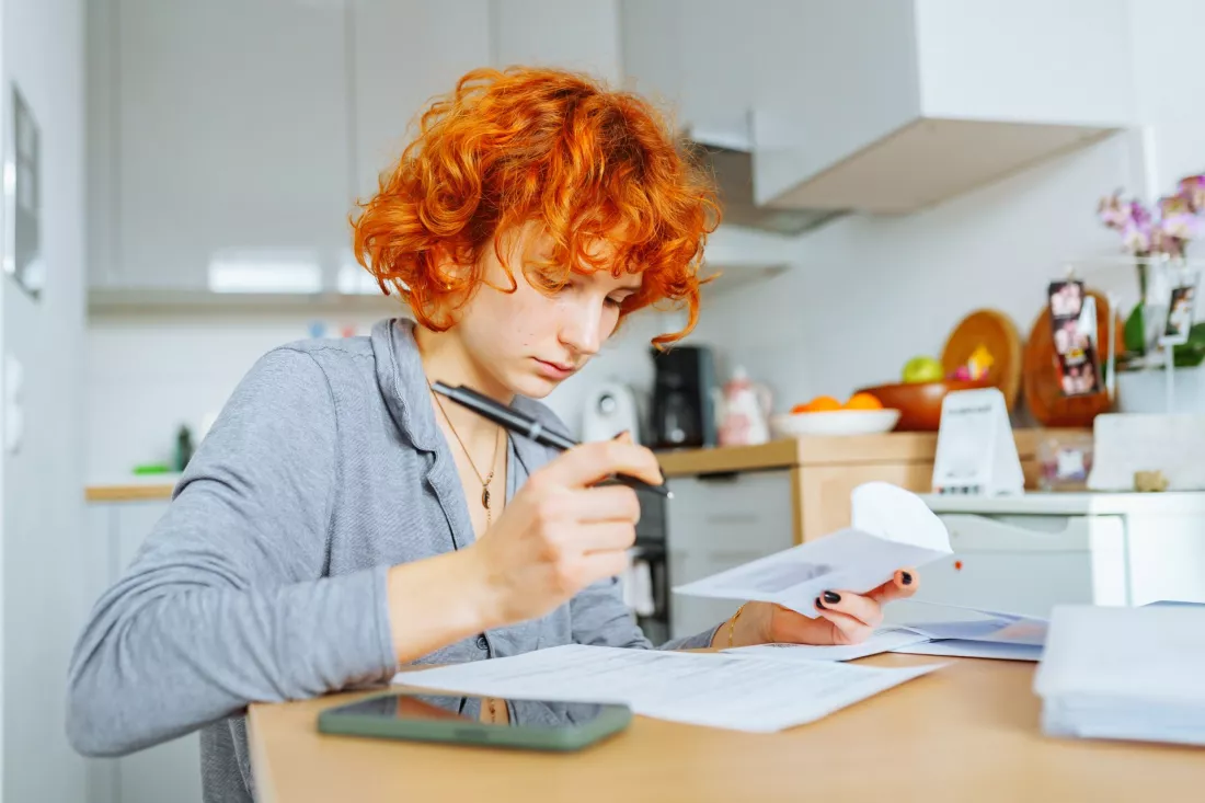 Studentka z rudymi wlosami wypelnia papierowy wniosek przy stole w kuchni