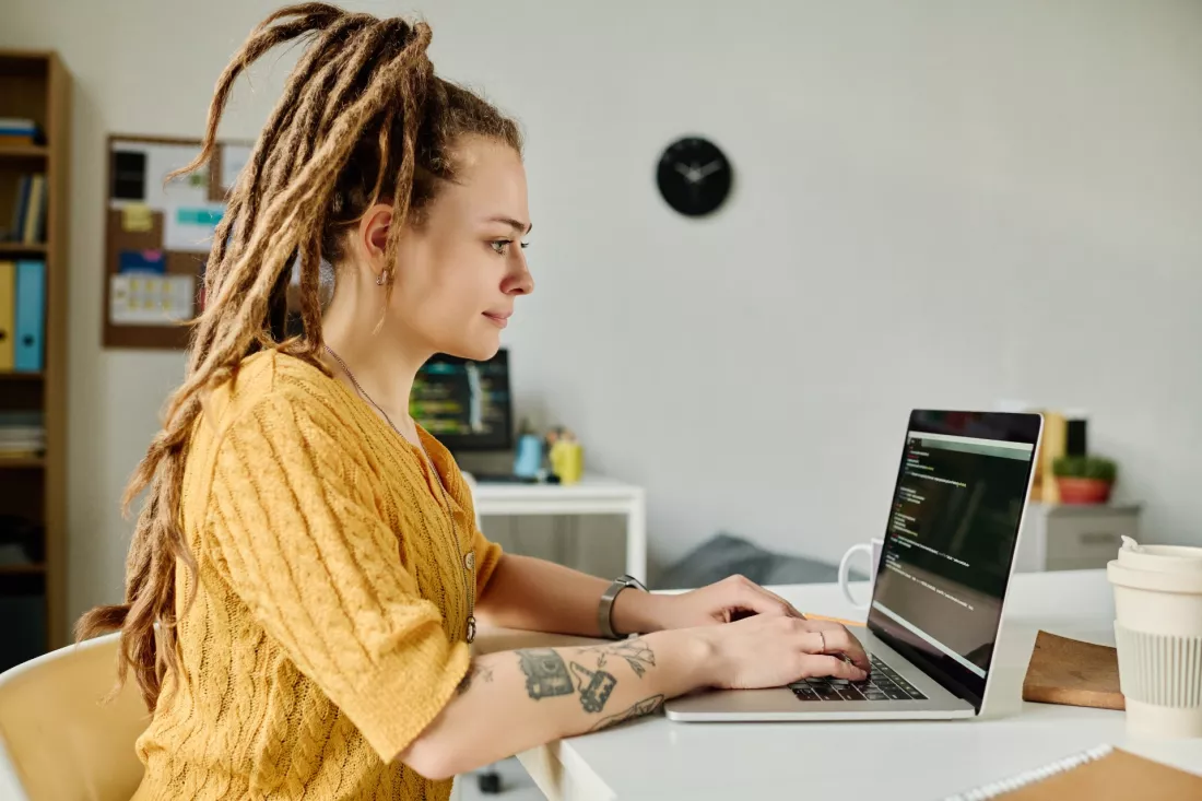 Mloda kobieta pisze kod na laptopie przy biurku