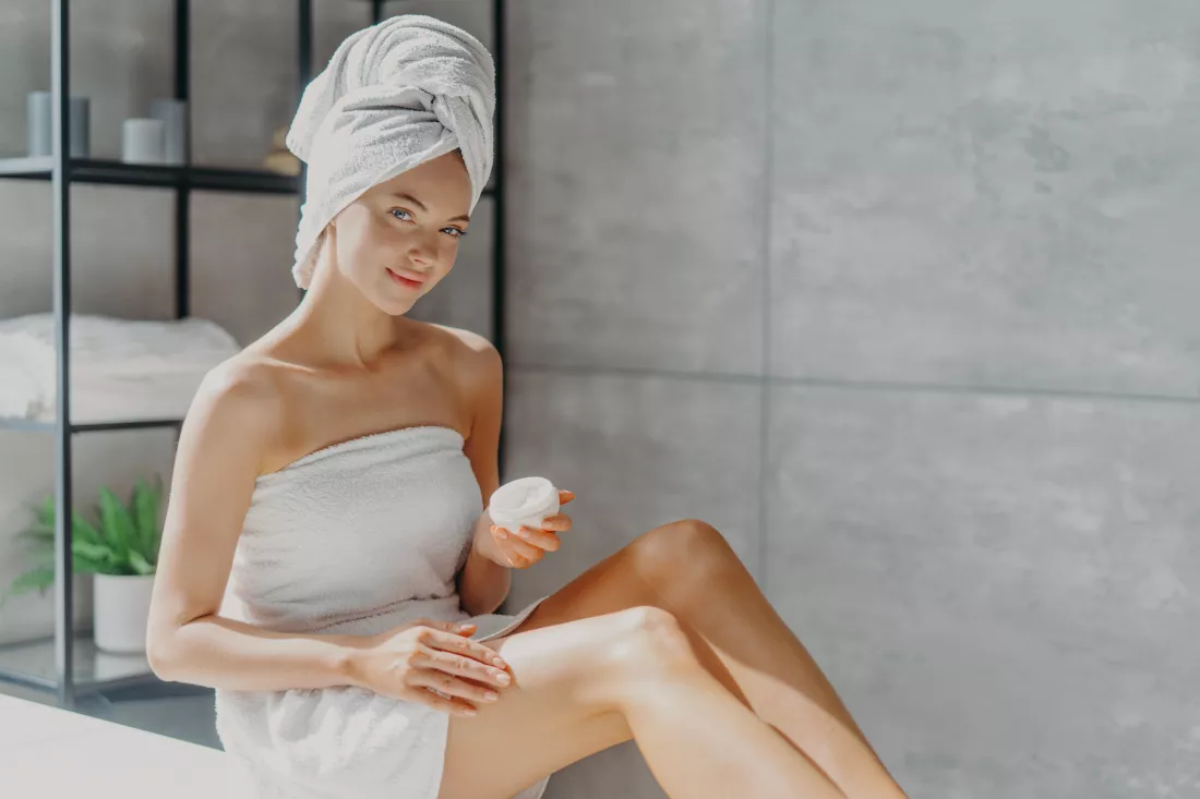 horizontal-shot-pretty-woman-applies-cosmetic-cream-skin-poses-wrapped-towel-undergoes-beauty-procedures-after-taking-shower-poses-home-bathroom